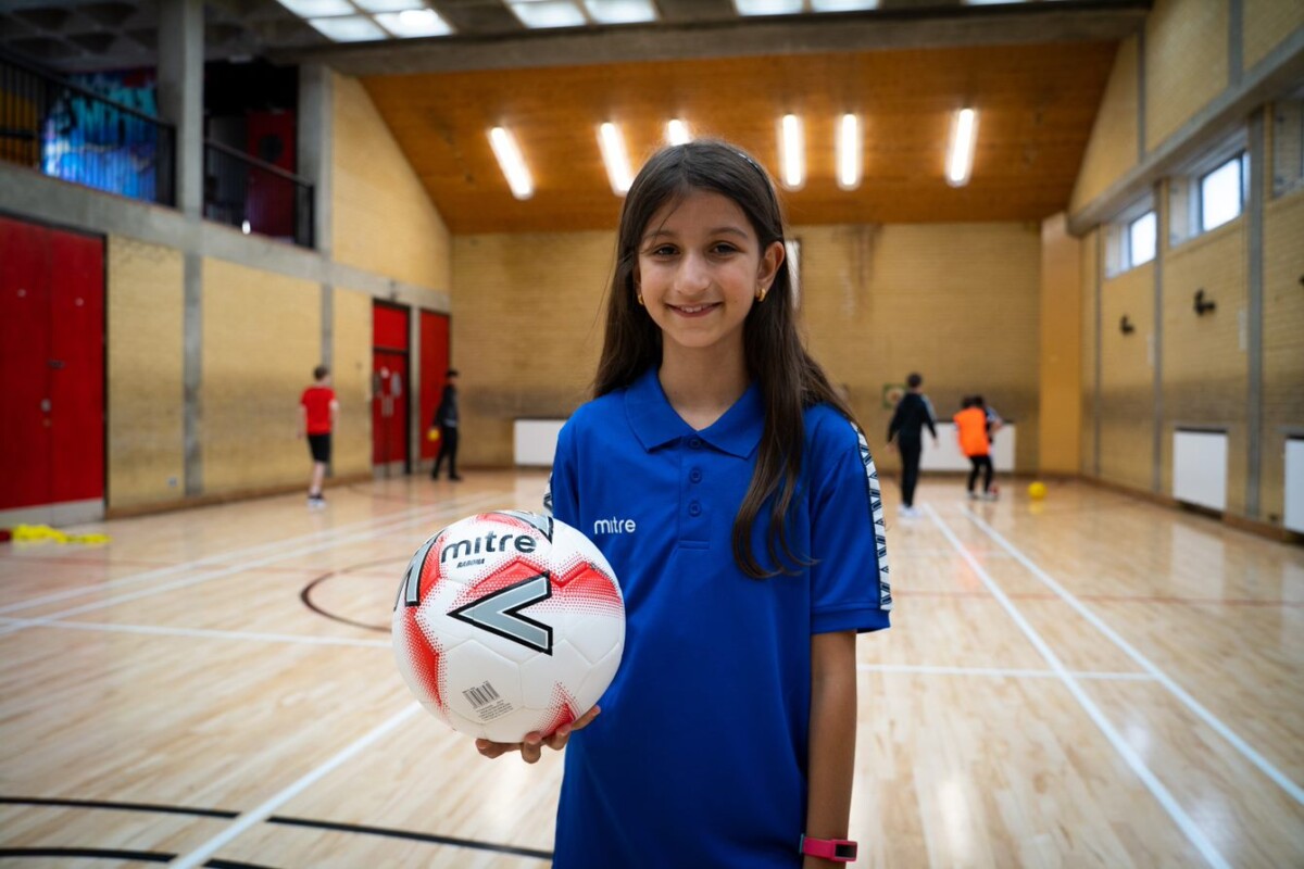 A girl smiles at the camera, holding a football