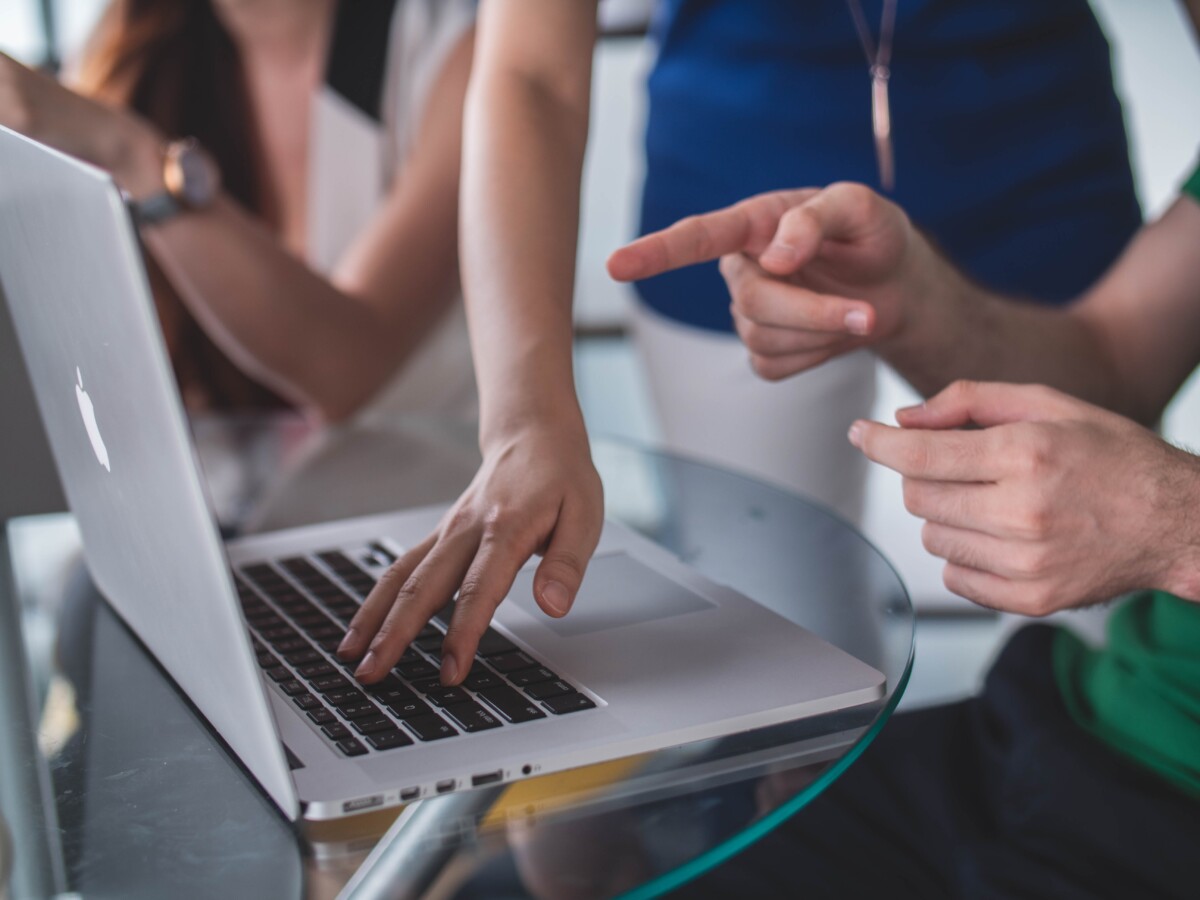 People at a laptop in a meeting, one touches the keys while another points at the screen. By Mimi Thian on Unsplash