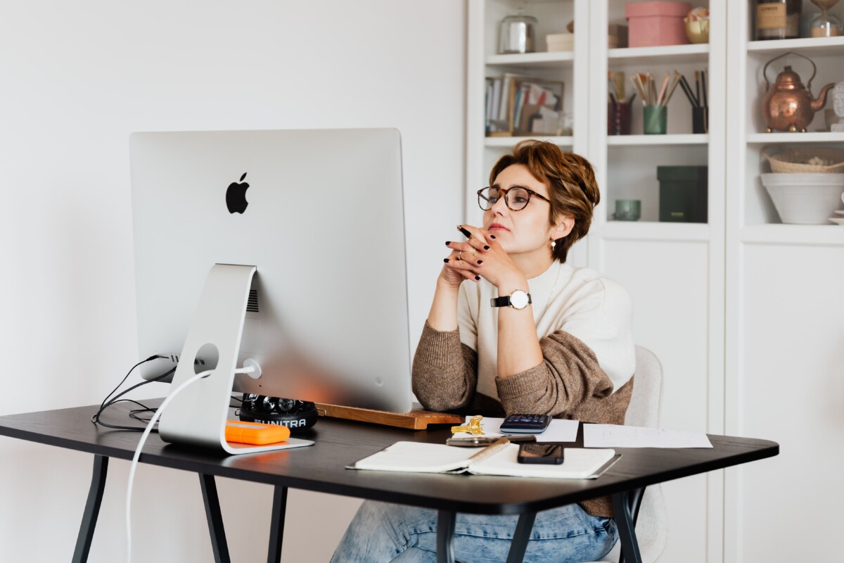 A woman in her 50s, in a thinking pose in front of her desktop computer. By Karoline Grabowska on Pexels