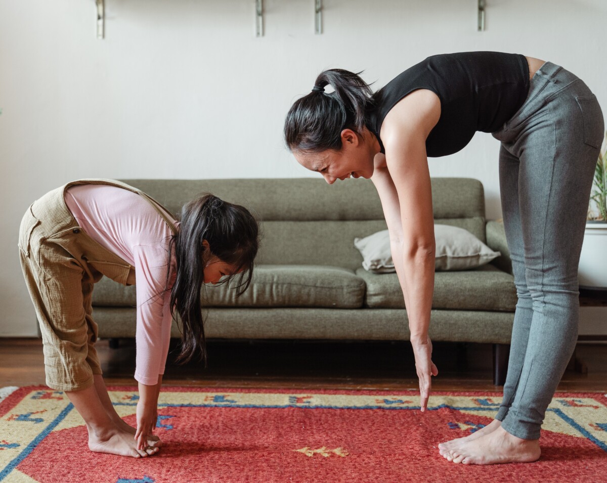 a woman and a girl try to touch their toes in front of a sofa. Photo by Ketut Subiyanto on Pexels