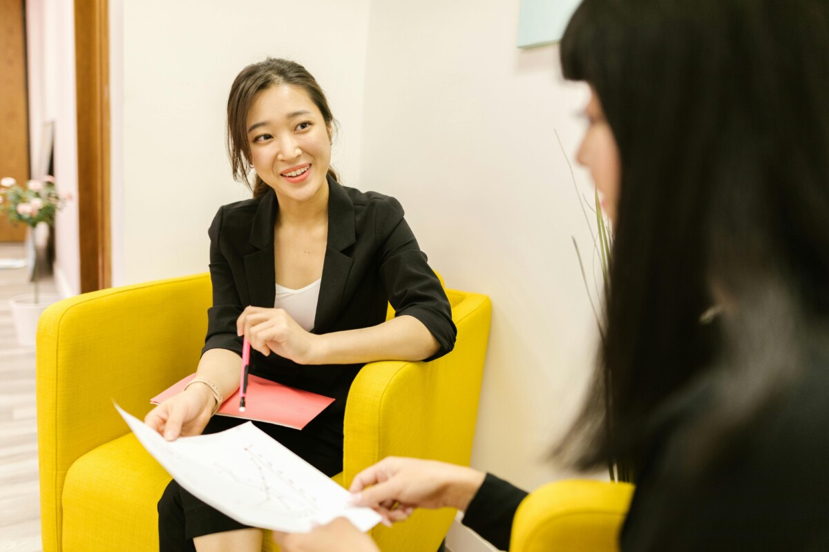 Two women in an office smile as they talk over some paperwork. By RDNE Stock project on pexels