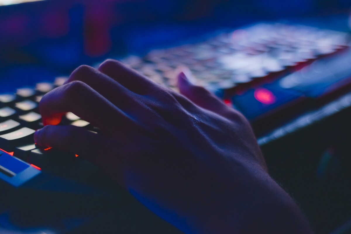 a hand types on a backlit keyboard in the dark