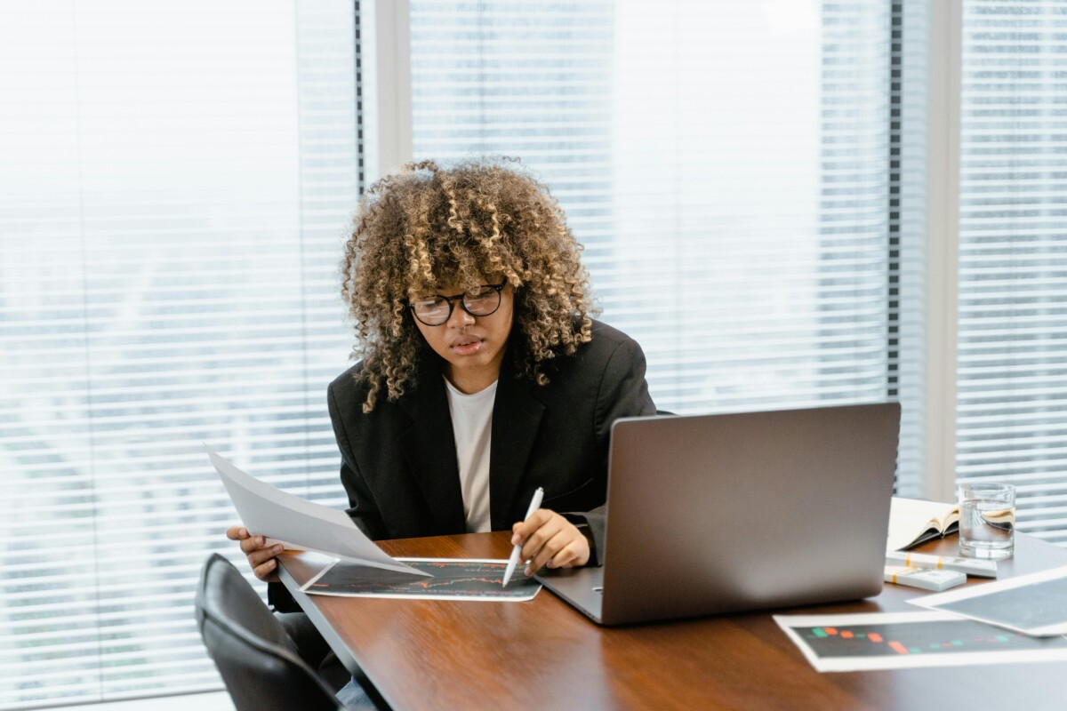 A business woman in an office pores over data at her desk. By Tima Miroshnichenko on pexels.